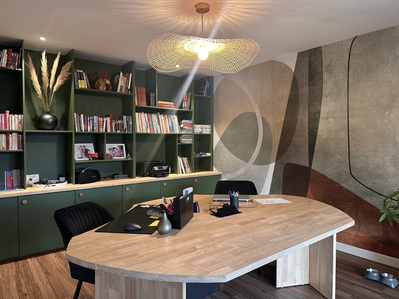 Bureau en bois aux formes organiques devant une bibliothèque verte et un papier peint panoramique